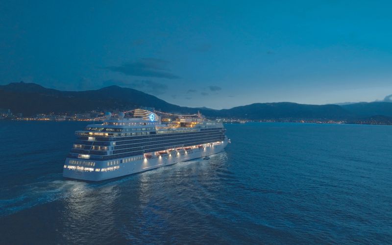 Brand new Allura cruise ship by Oceania Cruises cruising through sea with a vast mountain in the background