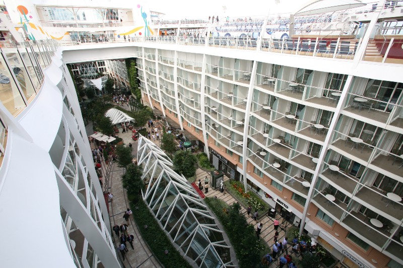 Overhead view of Allure of the Seas cruise ship's internal balcony staterooms overlooking a bustling central park area with guests and greenery.