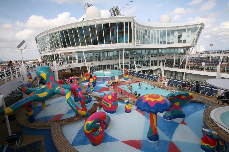 Colorful children's pool area on Allure of the Seas with whimsical water features and slides, surrounded by lounging areas under the watchful eyes of life guards, inviting for family fun at sea.