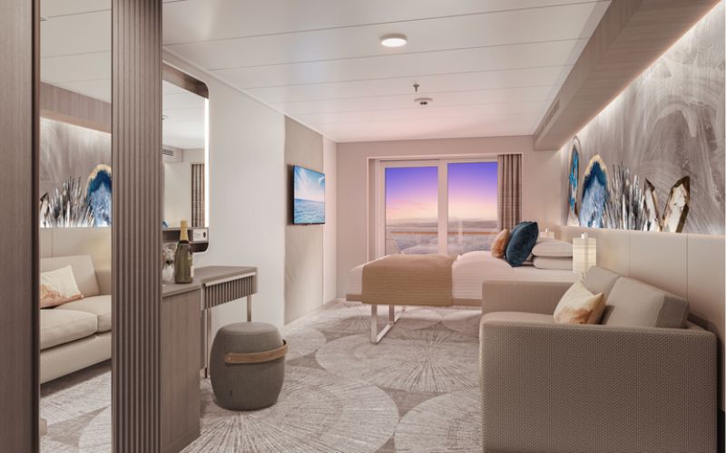 Luxurious cruise ship Balcony Stateroom interior with a view of the sunset through balcony doors, featuring a plush bed, comfortable seating area with a couch, a flat-screen TV, and elegant, modern decor with abstract art pieces.