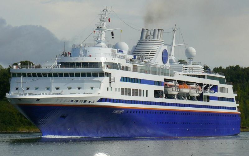 The Blue Dream Star cruise ship of Blue Dream Cruises, showcasing its vibrant blue hull and white superstructure, makes its way along a calm river flanked by greenery.