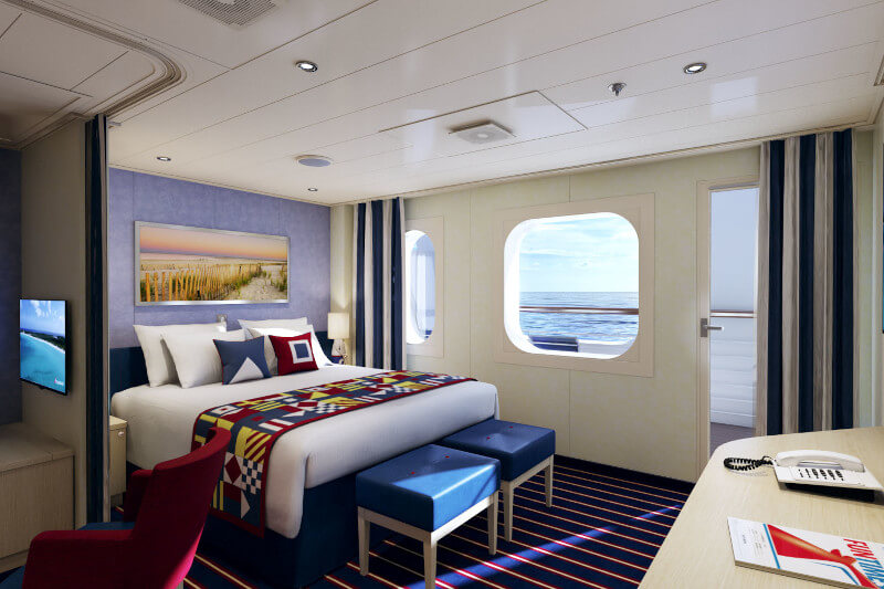 A spacious Family Harbor Suite on Carnival Vista, featuring a large bed with colorful geometric-patterned bedding, a porthole window with ocean views, and a cozy seating area, perfect for a family vacation at sea.