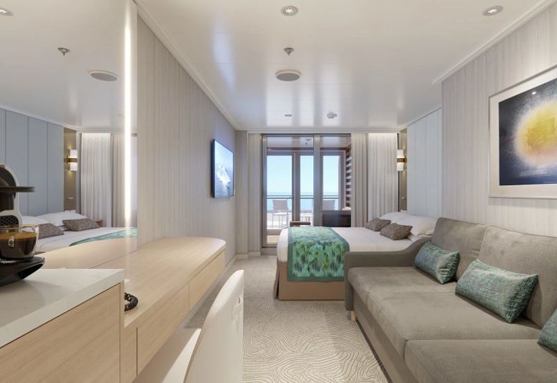The image shows a Cabana Mini-Suite on the Sun Princess. This suite features a cozy and stylish design with a large bed adorned with decorative pillows and a patterned bed runner. A comfortable sofa with matching pillows is positioned against the wall, providing a seating area. The room extends to a private balcony with outdoor seating, accessible through sliding glass doors, offering views of the ocean. The suite is equipped with a flat-screen TV mounted on the wall, a desk area with a mirror, and a coffee machine, all within a soft, neutral-toned decor that emphasizes luxury and relaxation.