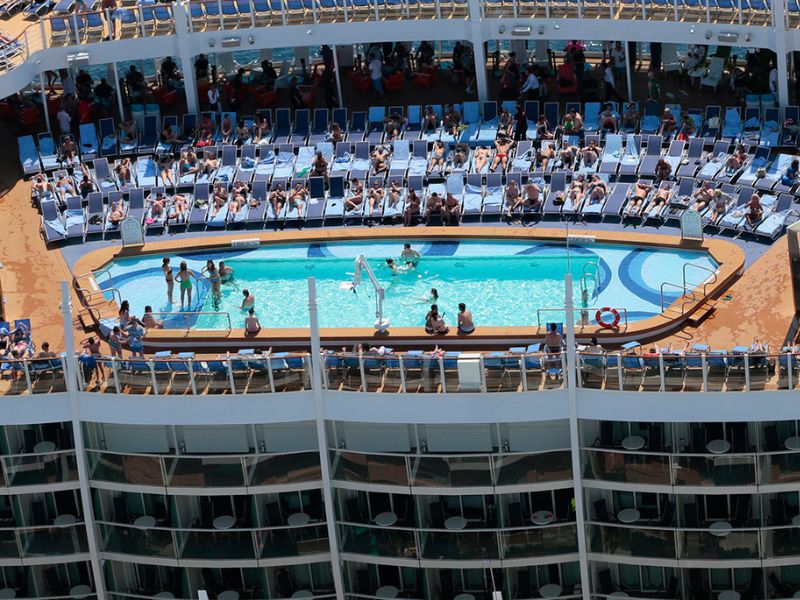 Overhead view of Harmony of the Seas' bustling pool deck, with guests swimming and lounging, directly above the ship's cabins, showcasing the close proximity to recreation areas.