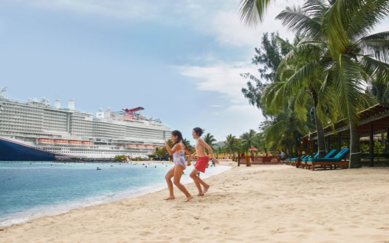 Two kids preparing to swim with a carnival cruise ship docked behind them