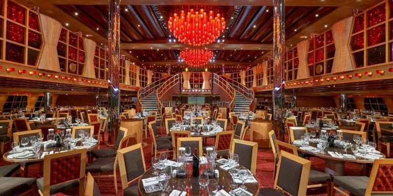 The grandiose main dining room of the Carnival Dream cruise ship, elegantly set for dinner with a symmetrical design, rich wooden accents, and a striking red chandelier as the centerpiece.