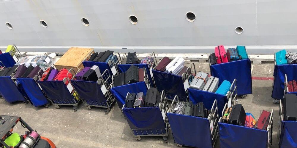 Rows of blue bins filled with colorful luggage lined up on the dockside ready for loading onto a Carnival Cruise ship, showcasing the organized process of handling guest belongings before departure.