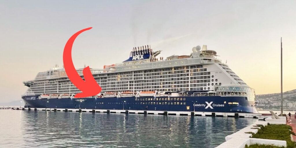 The Celebrity Apex cruise ship docked in port during sunset, with a large red arrow pointing towards the ship's bow against a backdrop of calm waters and a soft-hued sky.