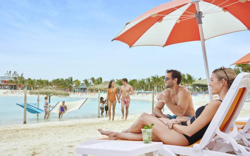 A man and woman sat next to a man at CoCo Cay on the beach.