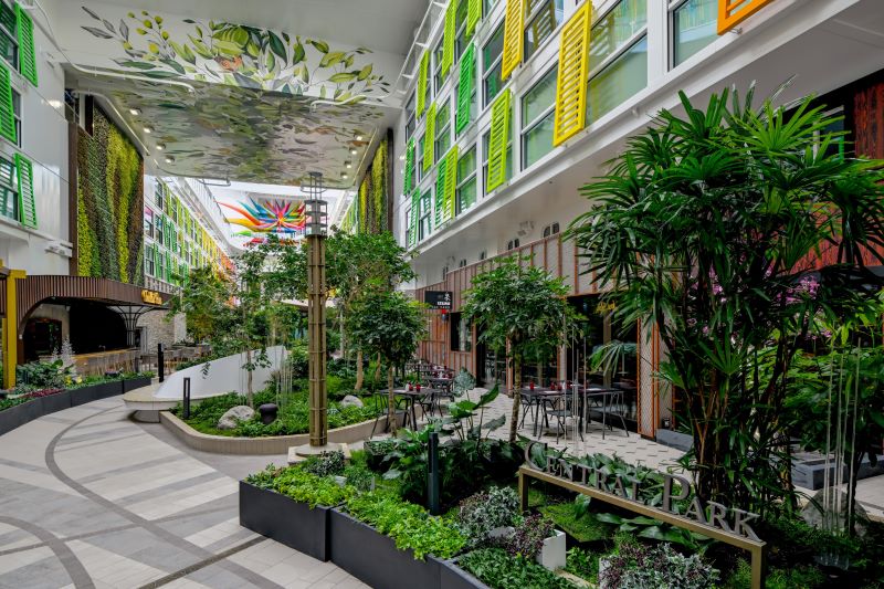 Central Park on Icon of the Seas features a serene, garden-like setting with lush greenery, winding pathways, and seating areas flanked by living walls and vibrant, shuttered balconies, offering a peaceful retreat amidst the liveliness of a cruise ship.