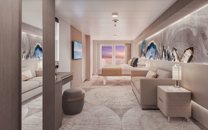 Elegant club balcony suite on a cruise ship during sunset, with a serene ocean view from the balcony, a beige daybed, a sofa with decorative pillows, abstract art on the walls, and stylish lamps providing a warm ambiance.