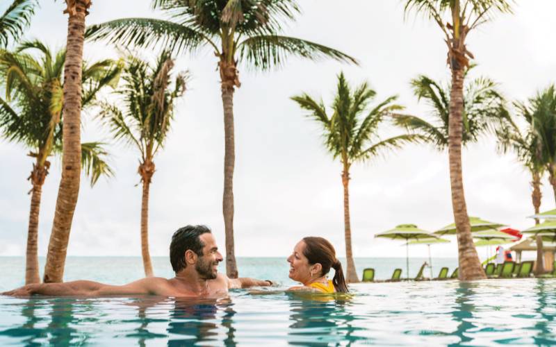 A man and a woman in an infinity pool, by the beach at coco cay.