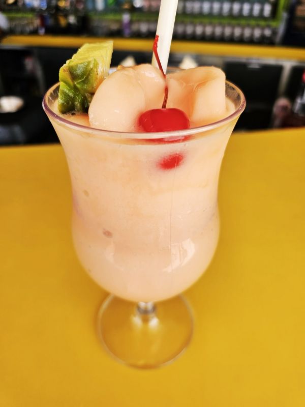 A Coco Loco cocktail on a Royal Caribbean cruise ship, served in a hurricane glass and garnished with a pineapple slice and cherry. The creamy, peach-colored drink is set against a bright yellow surface, with a bar area in the background, creating a vibrant and tropical atmosphere.