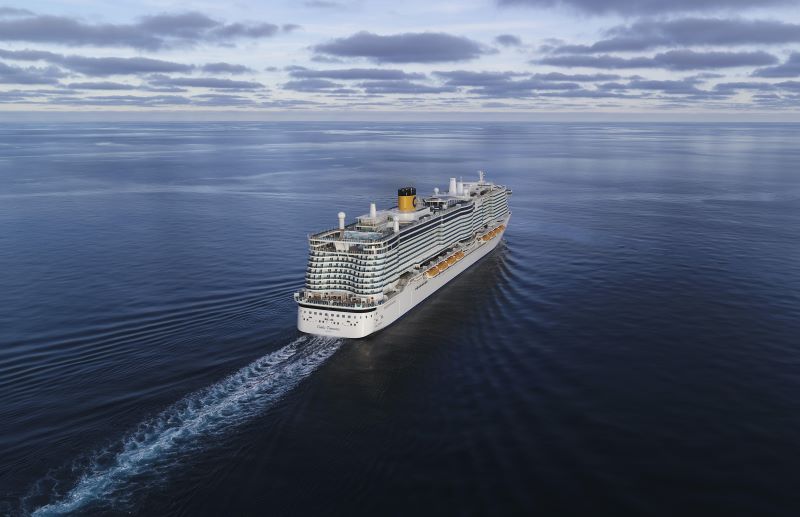 The Costa Toscana cruise ship is gliding through calm seas, captured from an aerial perspective. The ship's multiple decks with blue and white striped design, yellow lifeboats, and iconic yellow funnel with a 'C' logo are visible, contrasted against a tranquil marine backdrop with soft cloud cover.