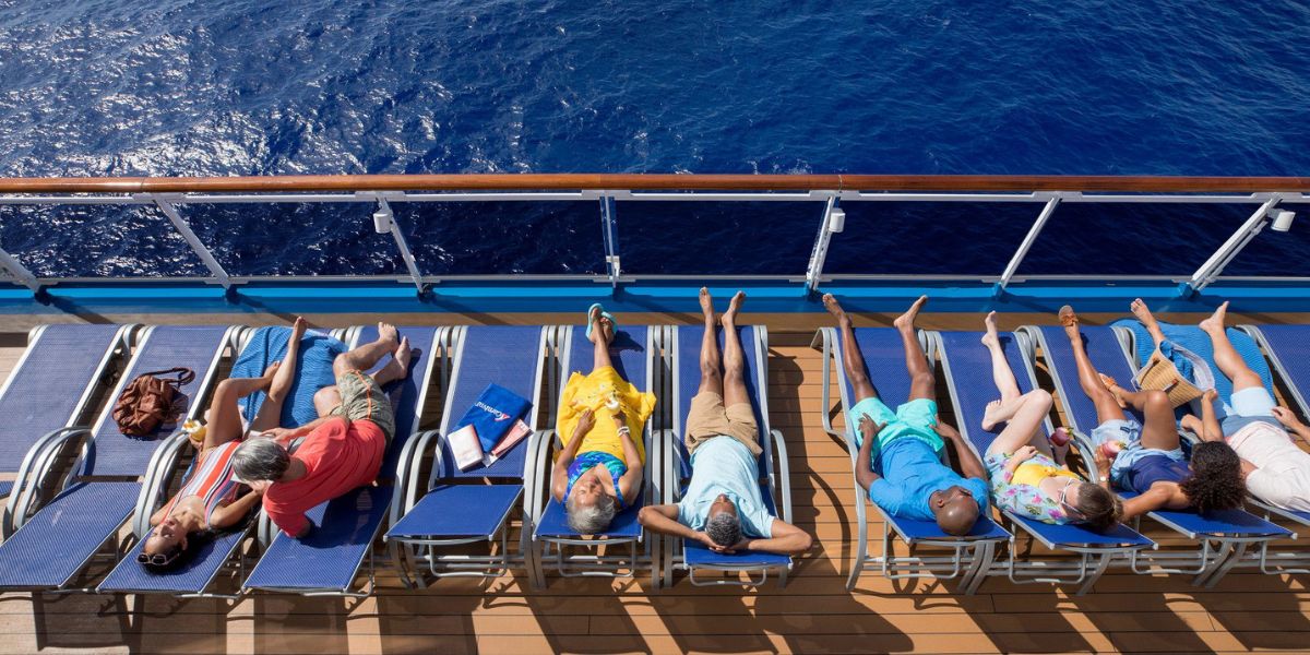 Passengers lounging on deck chairs aboard a Carnival Cruise Line ship, soaking up the sun with the deep blue sea beside them, embodying the relaxation and leisure of a day at sea.