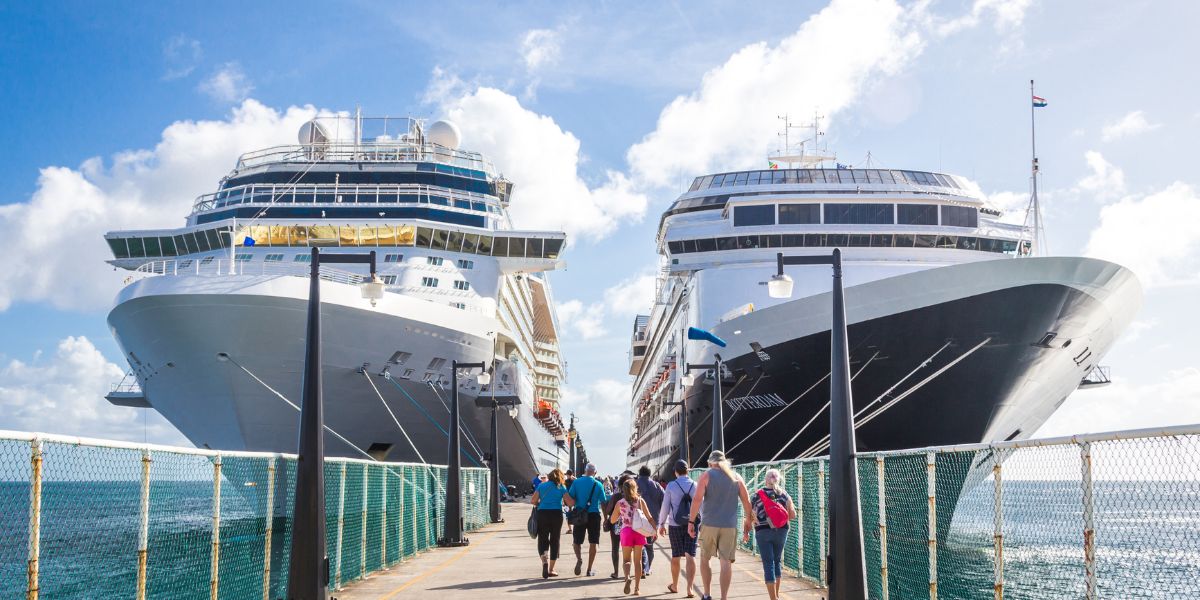 Two large cruise ships docked at a port under a clear blue sky. Passengers, visible as a group of diverse individuals including families and couples, are walking on the pier towards the ships. The scene captures a vibrant travel atmosphere, with the majestic cruise liners towering over the guests, symbolizing the start of a maritime adventure.