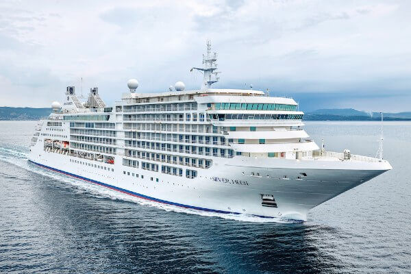 The Silver Moon cruise ship, from Silversea Cruises, sailing on calm waters with a cloudy sky in the background, showcasing the ship's white and blue livery and multiple decks.