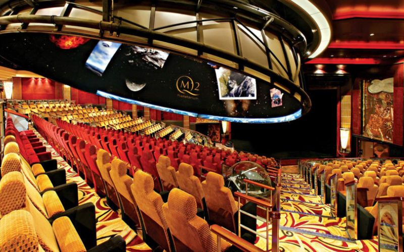 Inside the elegant planetarium on a Cunard cruise ship, with rows of comfortable seating under a dome featuring images of outer space, providing an educational and entertaining stargazing experience to guests at sea.