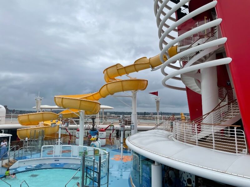 The Twist N Spout water slide on the Disney Magic cruise ship, spiraling above the pool deck under a cloudy sky, ready for vacationers seeking fun at sea.