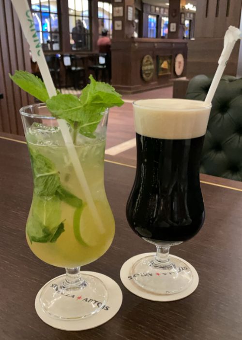 A refreshing mojito with fresh mint and a classic stout beer with a creamy head, both served on branded coasters in a traditional pub setting.