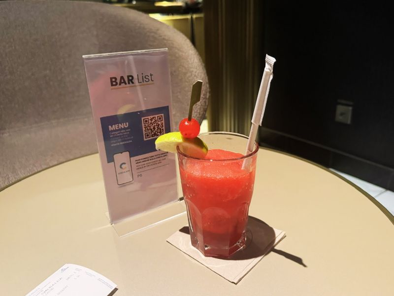 A refreshing strawberry daiquiri served in a rocks glass, garnished with a lime slice and a cherry, on a table with a bar list displaying a QR code menu, aboard the Costa Smeralda cruise ship.