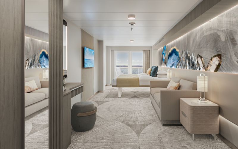Spacious family club balcony suite on a cruise ship, featuring a modern design with a comfortable bed, a large sofa, abstract wall art, a flat-screen TV, and a balcony offering a view of the sea under a soft sunset light.