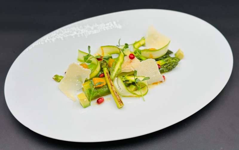 A delicately plated dish from Solis on a Seabourn cruise ship, featuring vibrant green asparagus spears, thinly sliced zucchini, red pepper accents, and shaved Parmesan cheese on an oversized white plate, embodying culinary elegance and simplicity.