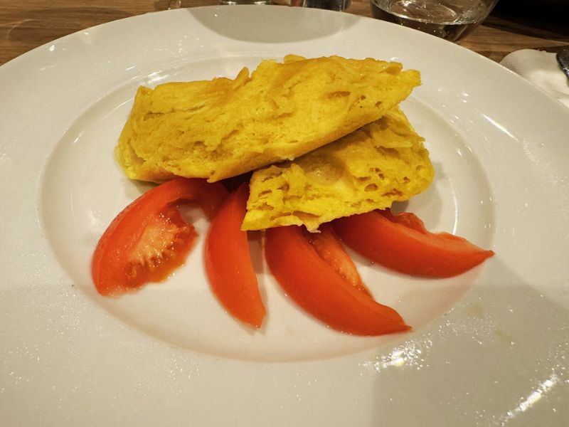 A simple yet appetizing dish of a golden folded omelet with slices of fresh tomato on the side, served on a white plate aboard the Costa Smeralda cruise ship.