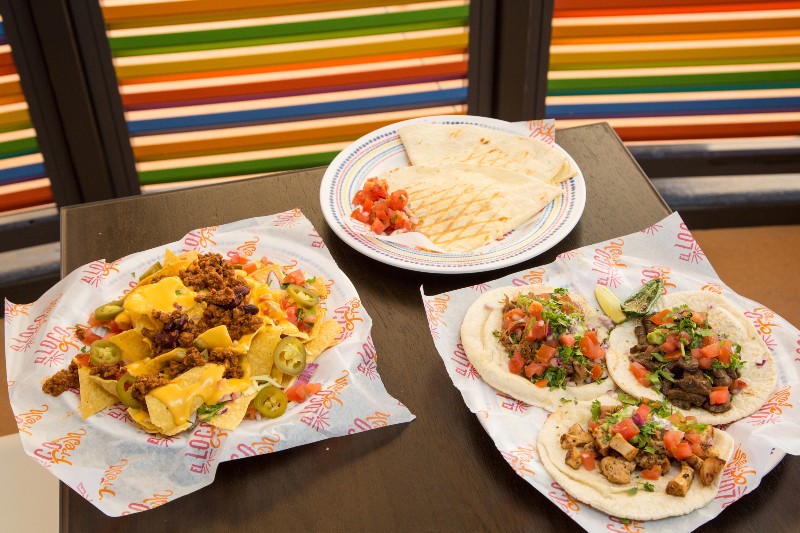 An appetizing array of Mexican food served on a Royal Caribbean cruise, featuring loaded nachos, a cheese quesadilla, and three soft tacos, presented on a table with a colorful striped backdrop.