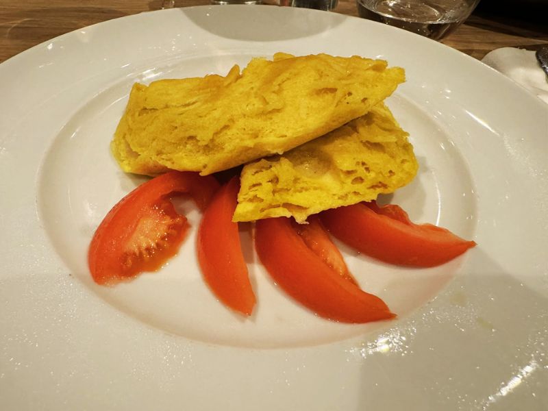 A traditional Italian omelette served with fresh tomato wedges, showcasing the authentic and fresh ingredients used in the Costa cruise ship's main dining room.