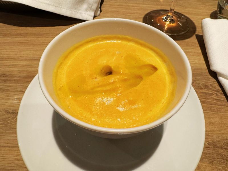 A vibrant orange pumpkin soup in a white bowl, indicative of the gourmet culinary offerings in the main dining room on the Costa cruise ship.