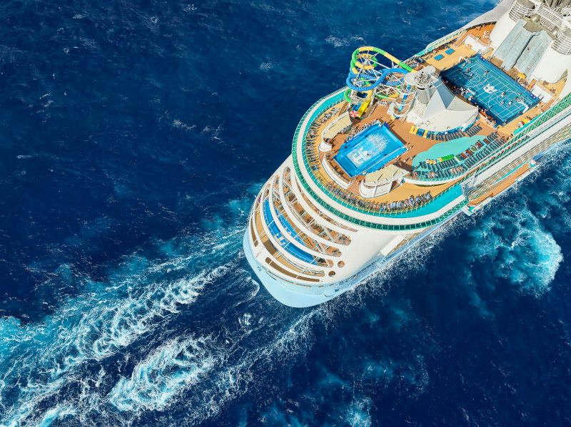 An overhead view of Royal Caribbean's Freedom of the Seas cruise ship sailing the deep blue ocean, featuring a bustling top deck with aqua-colored waterslides, swimming pools, and ample lounging areas for a fun-filled sea day.