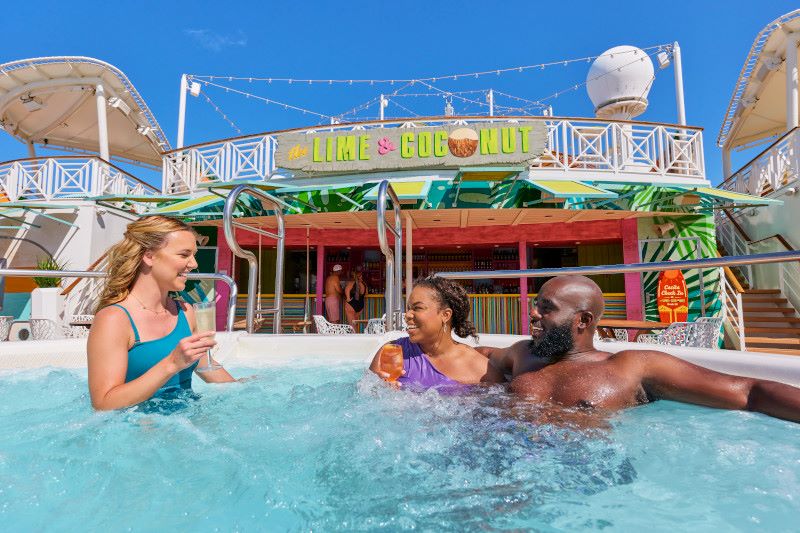 Three friends enjoy the vibrant poolside ambiance at the Lime & Coconut on Royal Caribbean's Freedom of the Seas. They're relaxing in the water with tropical drinks in hand, against the backdrop of a sunny sky, the ship's deck, and the colorful bar sign, encapsulating the ultimate cruise leisure experience.