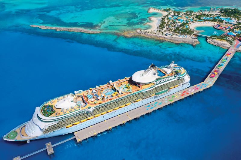 The aerial shot captures Royal Caribbean's Freedom of the Seas docked at the vibrant and picturesque CocoCay. The ship's deck is bustling with activities and amenities, while the crystal-clear Bahamian waters and the island's inviting beaches frame this idyllic cruise destination.