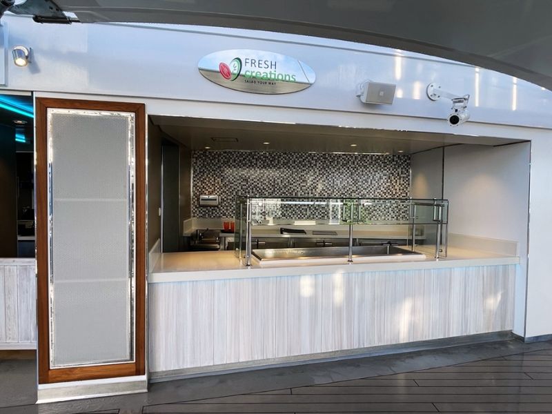 The 'Fresh Creations' salad bar on the Carnival Celebration cruise ship, featuring a clean and modern serving counter with a mosaic tile backsplash, waiting to offer guests custom salad creations in a bright and inviting setting.