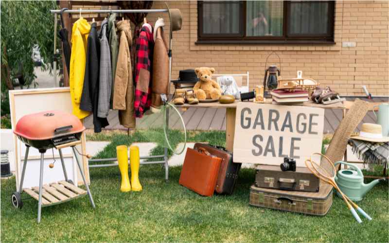 A garage sale in a garden, selling clothes and other items.