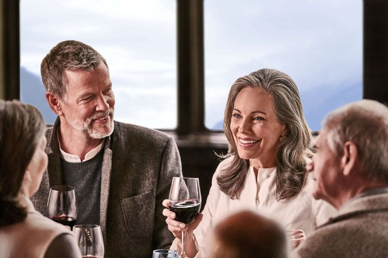 A group of guests enjoying a sociable moment with wine glasses in hand on Princess Cruises, with a couple engaging in a cheerful conversation, embodying the warm, convivial atmosphere of the cruise experience.