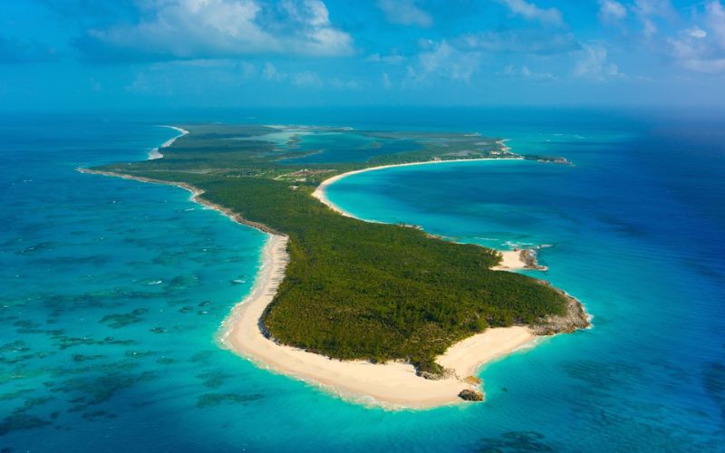 Aerial view of Half Moon Cay, revealing its crescent-shaped shoreline nestled in the heart of a serene blue sea. The lush greenery of the island contrasts with the soft white sands, creating a picturesque and tranquil tropical paradise.