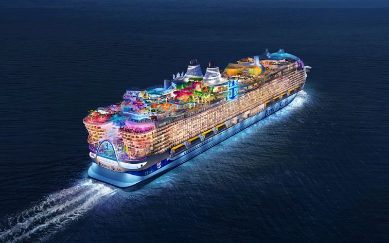 Aerial view of Royal Caribbean's 'Icon of the Seas' cruise ship, displaying its colorful deck attractions, including water slides and pools, as it navigates through the ocean with its name prominently displayed on the bow.