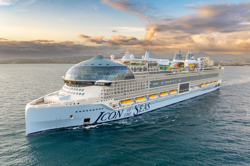 Royal Caribbean's Icon of the Seas luxury cruise ship sailing at dusk, with its name visible on the hull and a calm sea in the background.