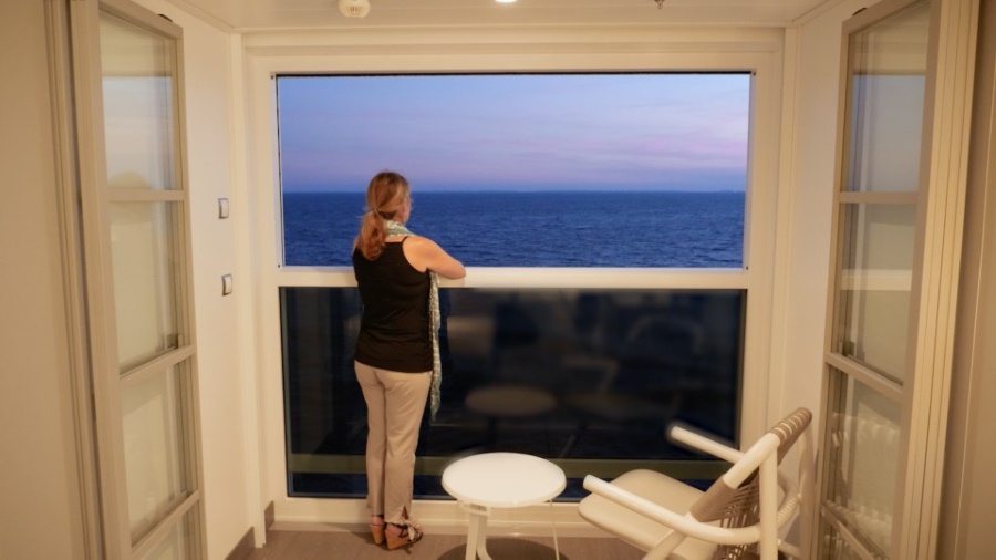 A guest enjoying the serene ocean view from the Infinite Verandah on a Celebrity cruise ship, featuring a spacious windowed balcony with modern outdoor furniture.