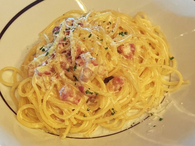 A tantalizing plate of spaghetti carbonara, richly coated with a creamy sauce and dotted with pieces of pancetta, sprinkled with grated cheese and parsley, ready to be enjoyed at La Cucina on NCL Getaway.