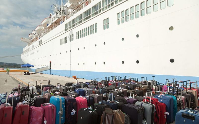 Large group of suitcases with cruise ship in the background