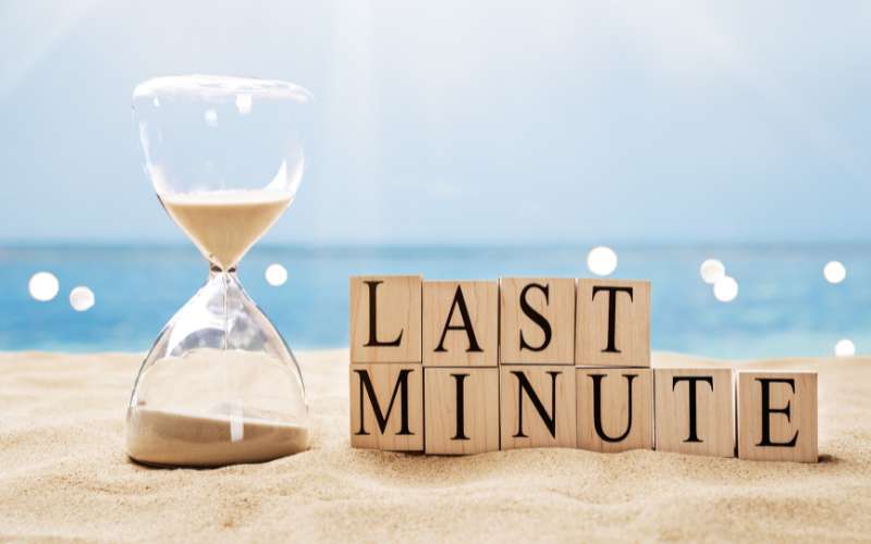 An hourglass on a beach, with the letters of "last minute" printed on each one.