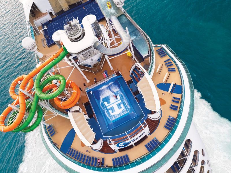 An aerial view showcases the dynamic and colorful waterslides of Liberty of the Seas, twisting above the ship's deck. Below, the deep blue sea rushes past, framing the ship's bustling activity areas, including the pools and lounging decks, inviting a sense of adventure and relaxation on the high seas.