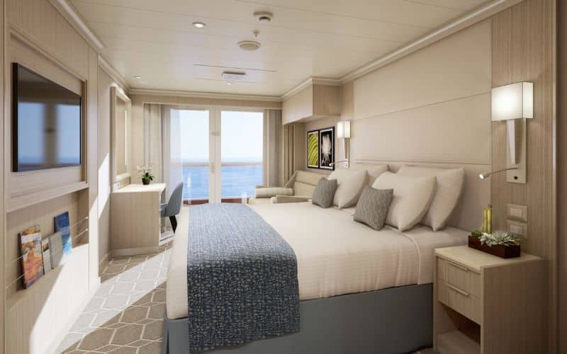 A serene Spa Stateroom on MS Rotterdam featuring a comfortable king-size bed with neutral-toned bedding, a sitting area by the balcony doors, and a tranquil ocean view.