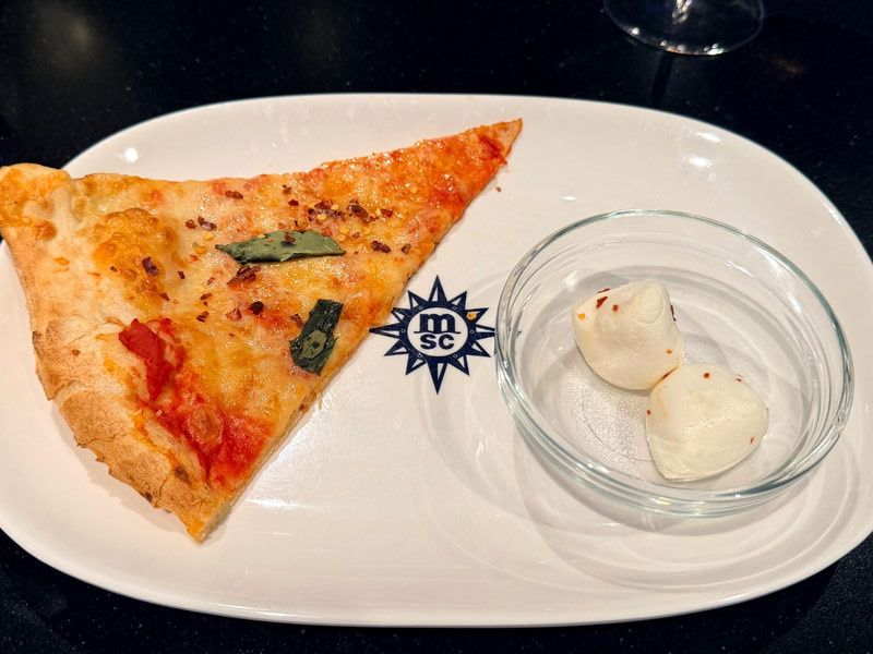 A slice of pizza and some mozzarella balls on an MSC Cruises-branded plate.