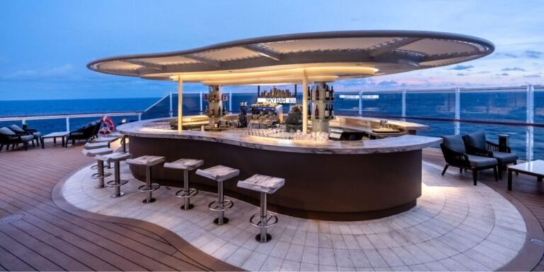Elegant outdoor bar on a cruise ship deck at dusk, with a modern circular bar setup and stools overlooking the calm sea.