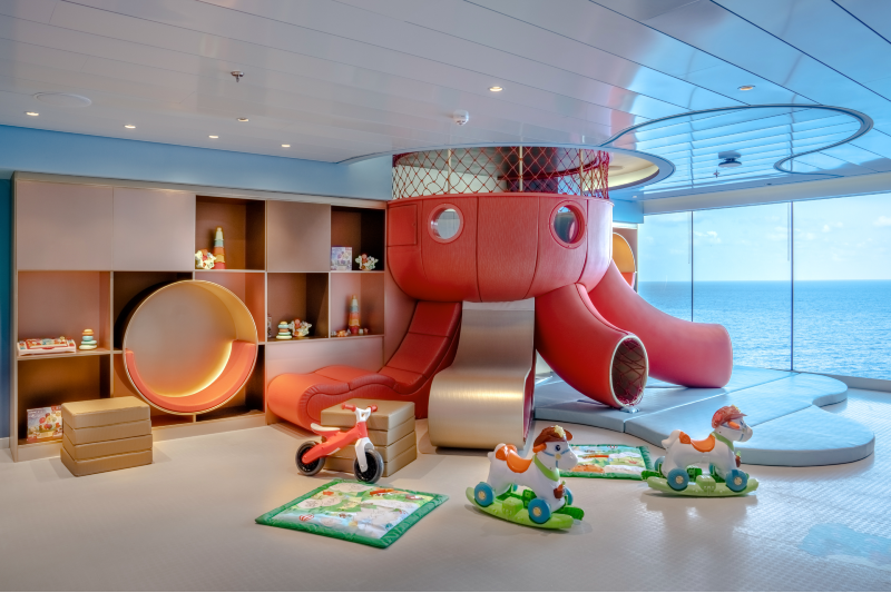 The Baby Club on MSC World Europa, a playful and secure area for toddlers, with bright colors, a large red octopus slide, interactive toys, and an ocean view, providing a fun and engaging environment for the youngest guests on board.