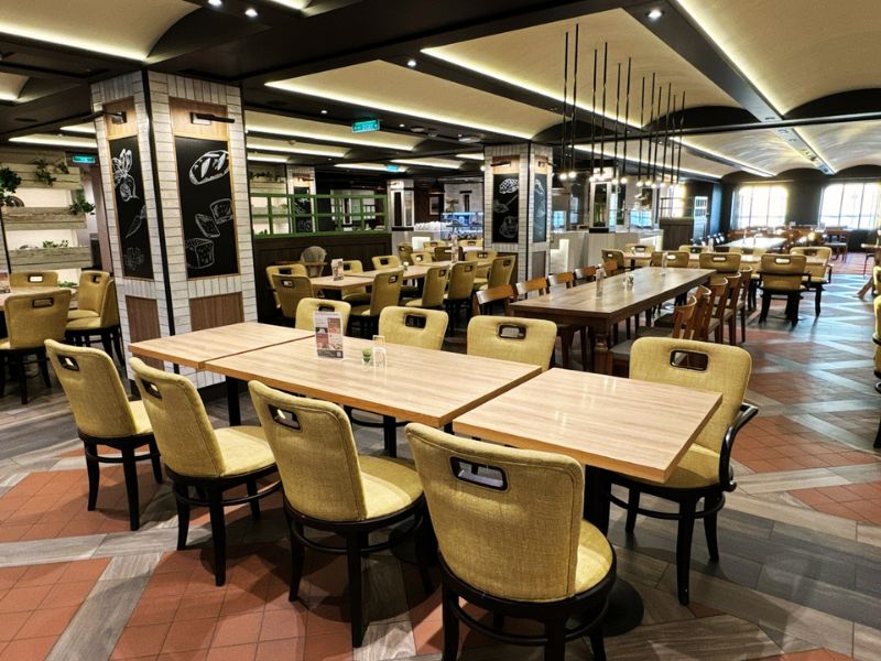The main dining room on the Costa Smeralda cruise ship, featuring elegant wooden tables and chairs, decorative lighting, and a welcoming, spacious layout ready to host guests for a meal.